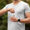 A person wearing a white t-shirt is holding a clear glass of water and a smartwatch on their wrist.