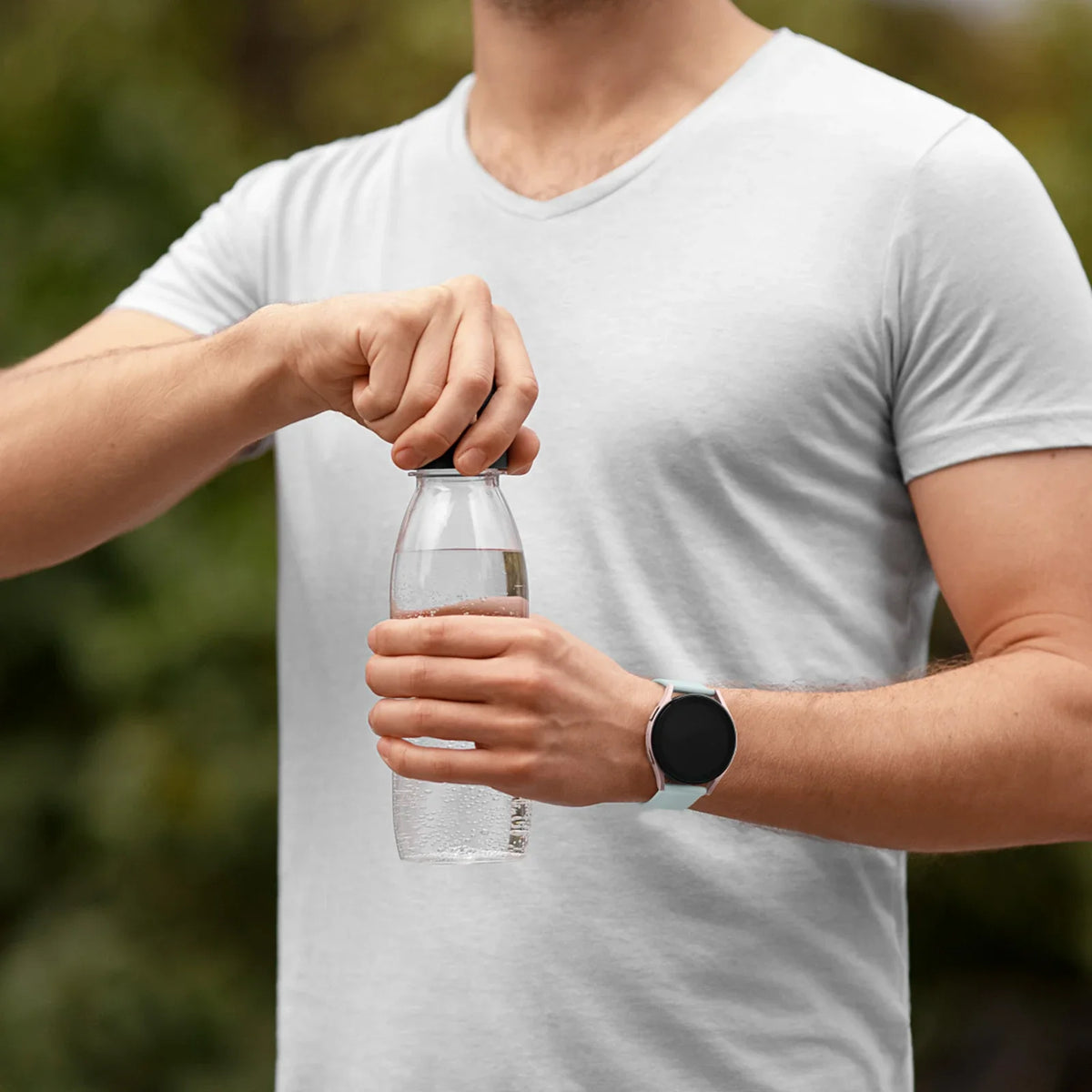 A person wearing a white t-shirt is holding a clear glass of water and a smartwatch on their wrist.