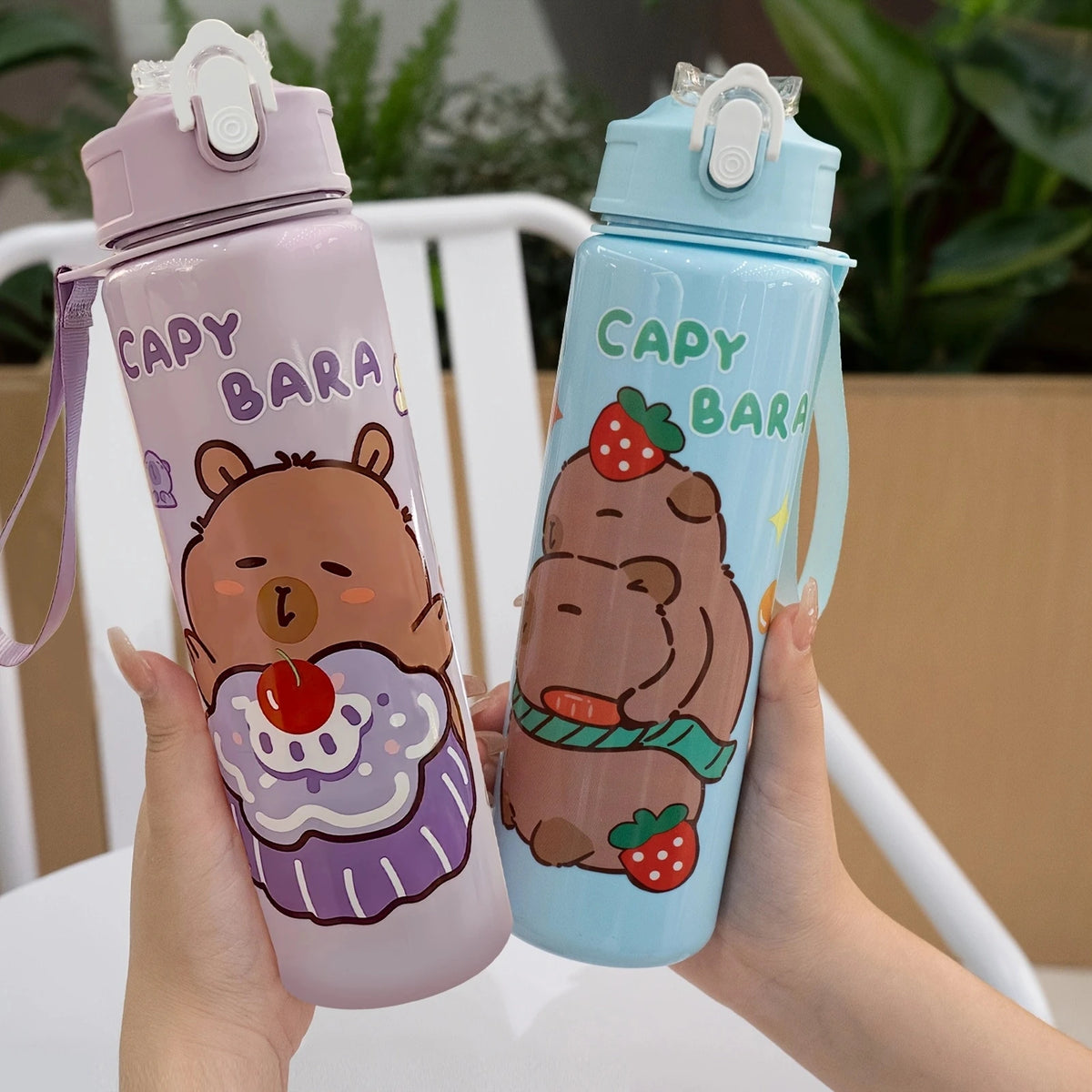 A person holds a purple cartoon drinking water bottle with a straw and a light blue cartoon drinking water bottle with a stra