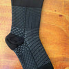 Black therapeutic compression socks with a patterned design laid on a wooden surface.