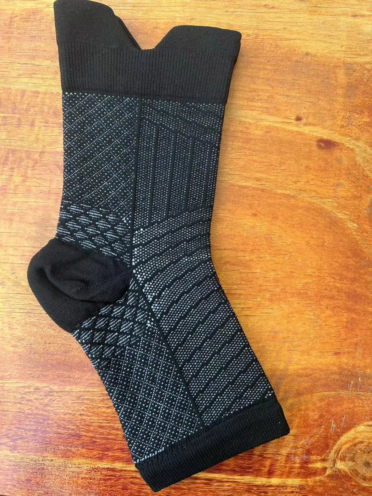 Black therapeutic compression socks with a patterned design laid on a wooden surface.