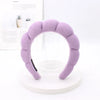 A lavender sponge terry cloth headband for hair styling displayed on a white stand.