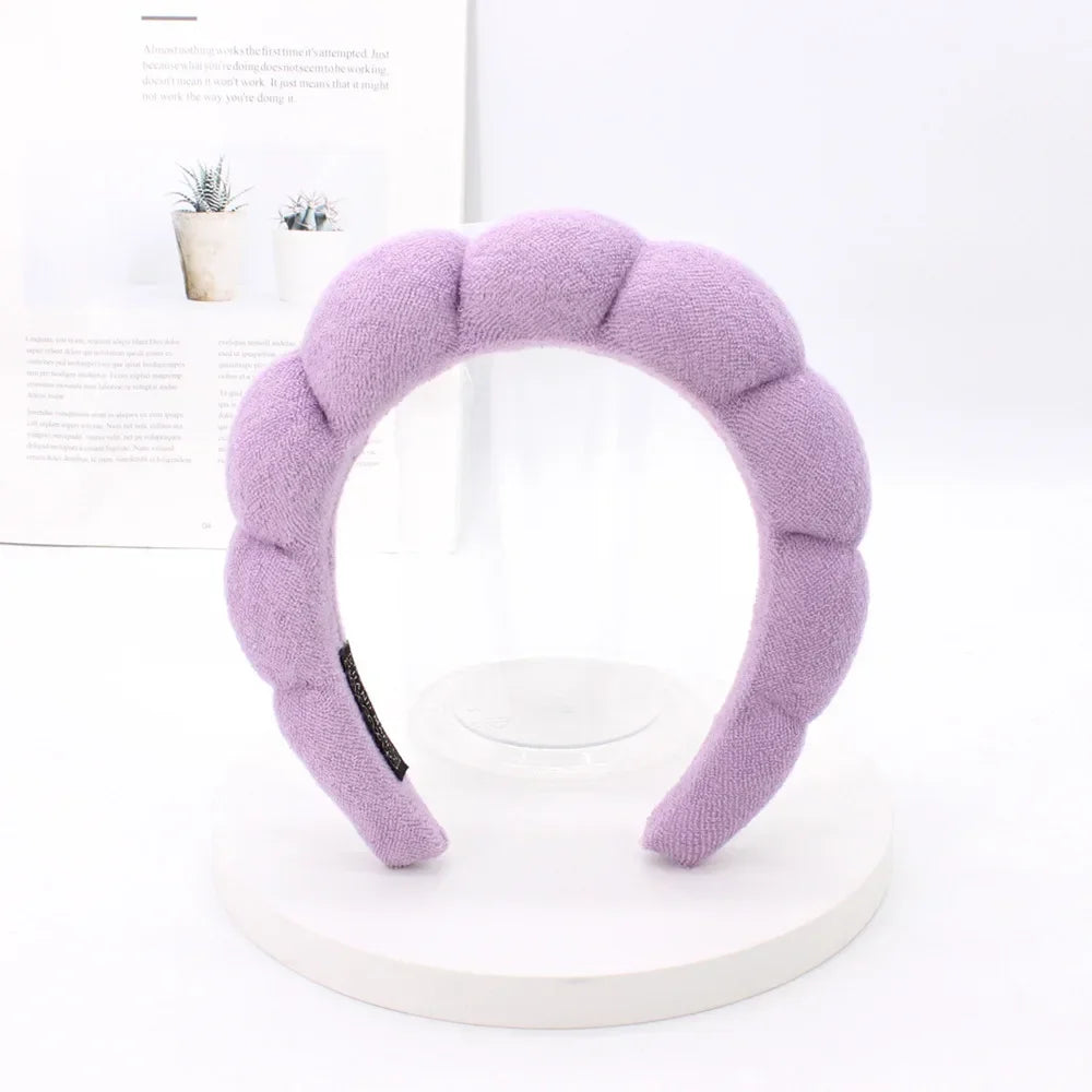 A lavender sponge terry cloth headband for hair styling displayed on a white stand.