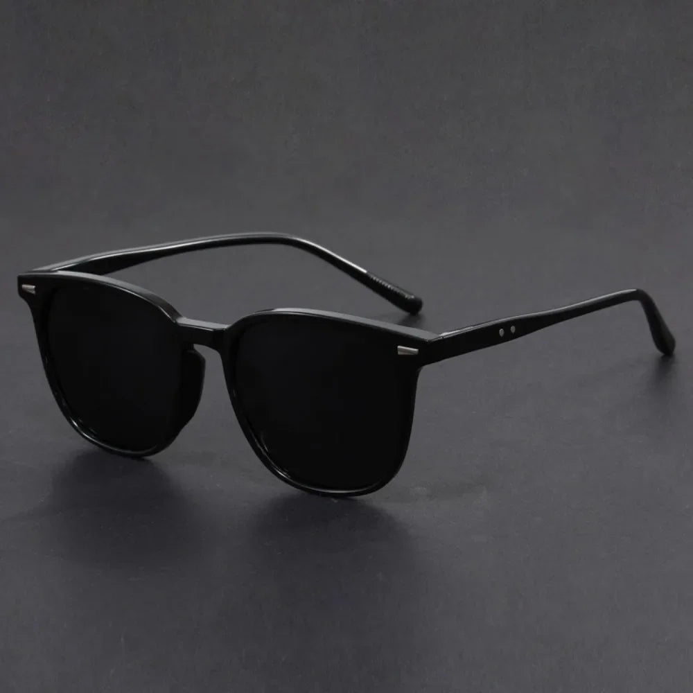 Black square sunglasses with thin arms resting on a dark surface.