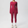 A woman wearing a long-sleeved maroon performance yoga and gym set with matching leggings and white athletic shoes.