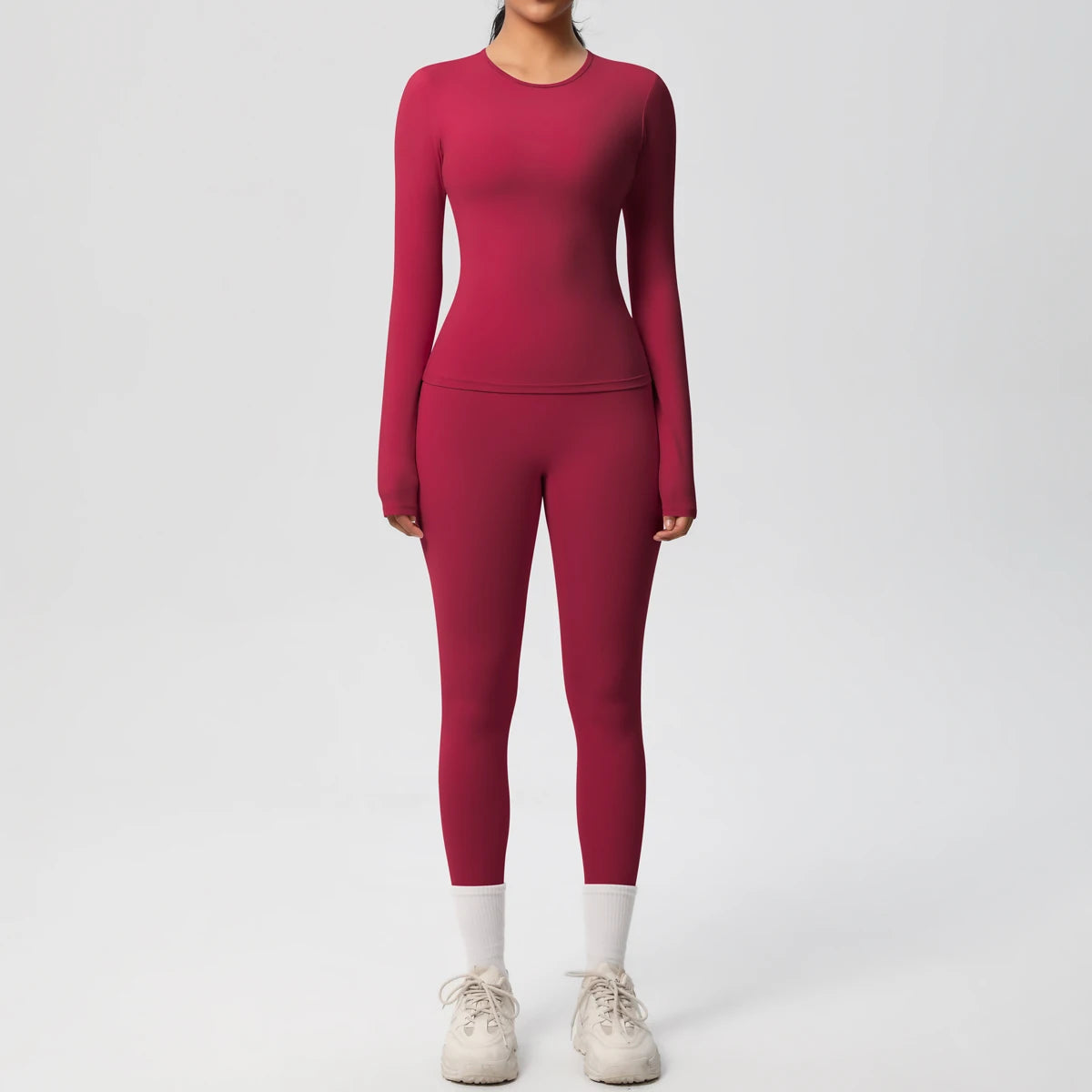 A woman wearing a long-sleeved maroon performance yoga and gym set with matching leggings and white athletic shoes.