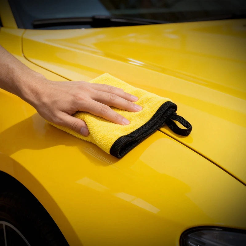 A hand is wiping a bright yellow car surface with a yellow microfiber cloth.