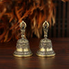 Une paire de cloches ou de maracas en bronze orné avec des ornements, posées sur une surface en bois sombre.