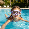 A smiling young girl wearing purple swimming goggles is floating in a bright blue pool.