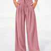 A model wears dusty rose flowy high waist drawstring wide leg pants with a white cropped top.