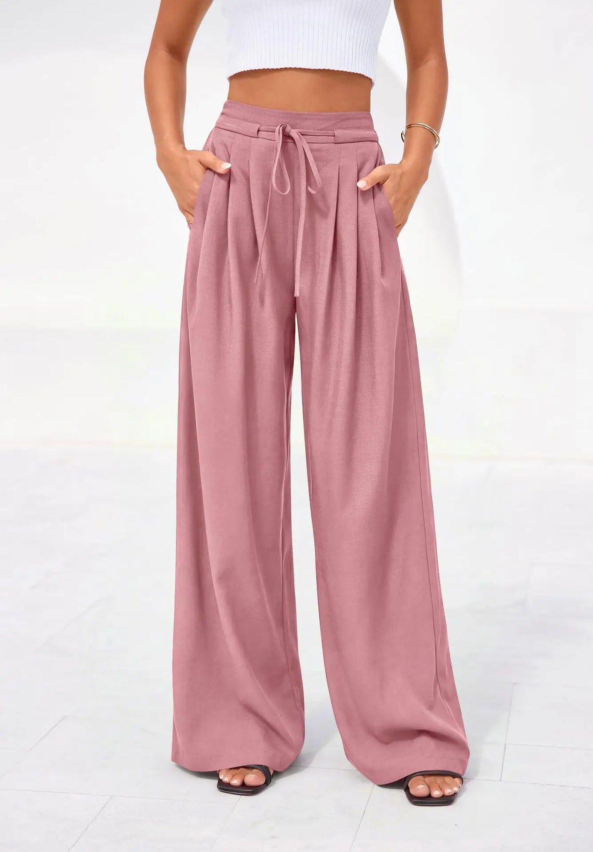 A model wears dusty rose flowy high waist drawstring wide leg pants with a white cropped top.