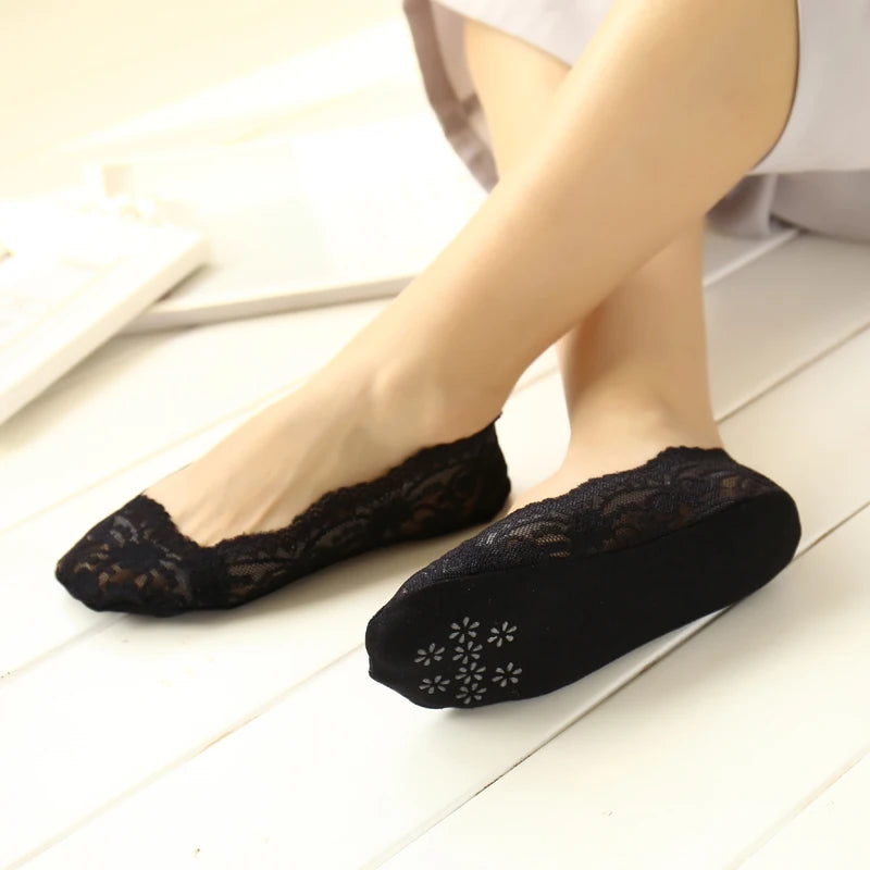 Calcetines de silicona de encaje negro sin dedos puestos en el pie de una mujer contra una superficie de madera blanca.