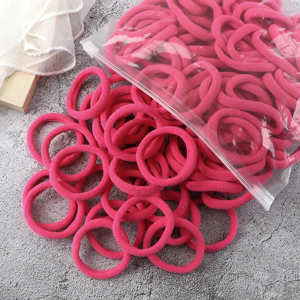 A pile of pink and red elastic hair bands is displayed on a gray surface.