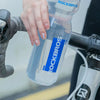 A hand is holding a clear plastic sports water bottle with the ROCKBROS logo on it.