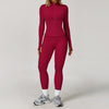A woman wearing a long-sleeved maroon yoga sports set with matching leggings and white socks, standing against a light backgr