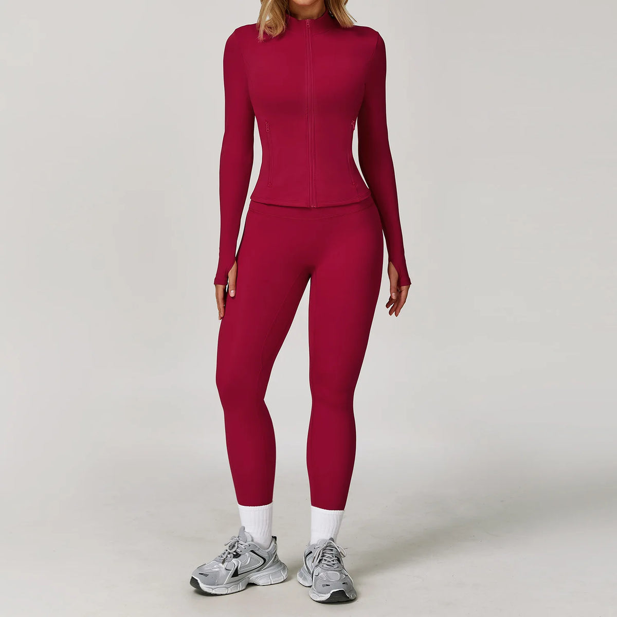 A woman wearing a long-sleeved maroon yoga sports set with matching leggings and white socks, standing against a light backgr