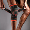A person's lower leg is wrapped in a black and orange breathable compression knee brace for joint support.