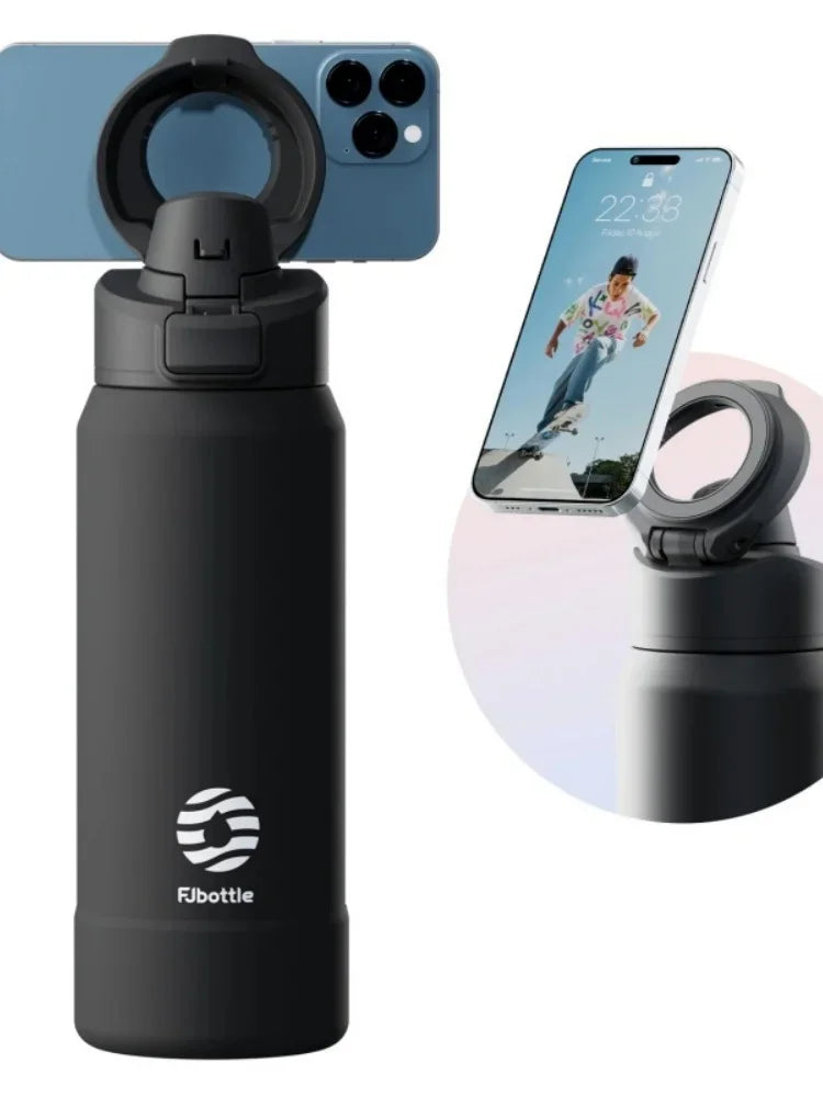 A black insulated sports water bottle with a magnetic lid is shown next to a smartphone displaying a picture of a person jump