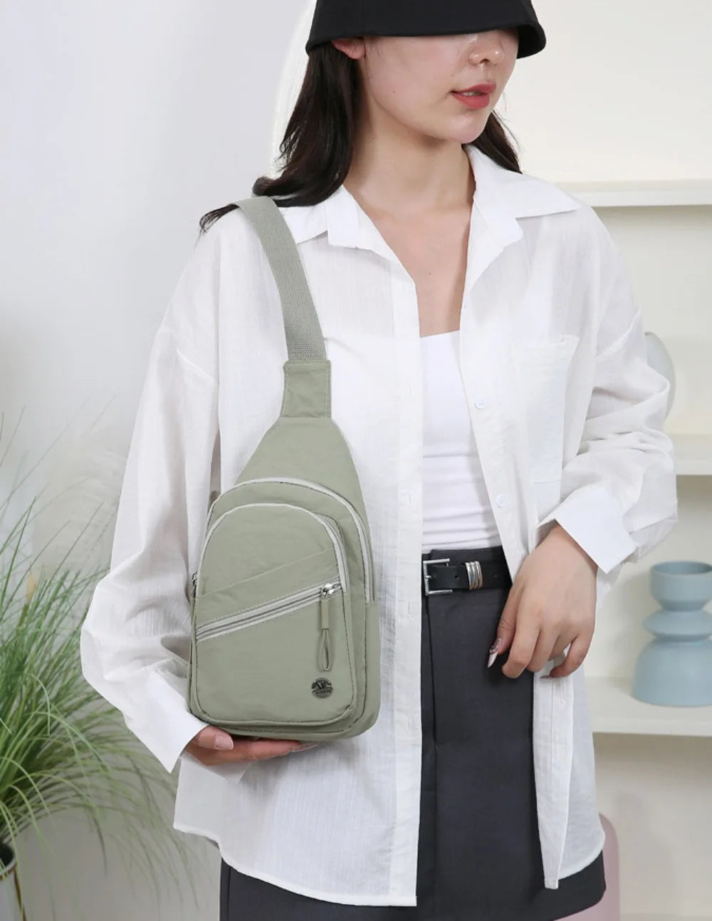 Eine Frau hält eine hellgrüne strapazierfähige Crossbody-Messenger-Tasche vor einem weißen Hemd und einem dunklen Rock.
