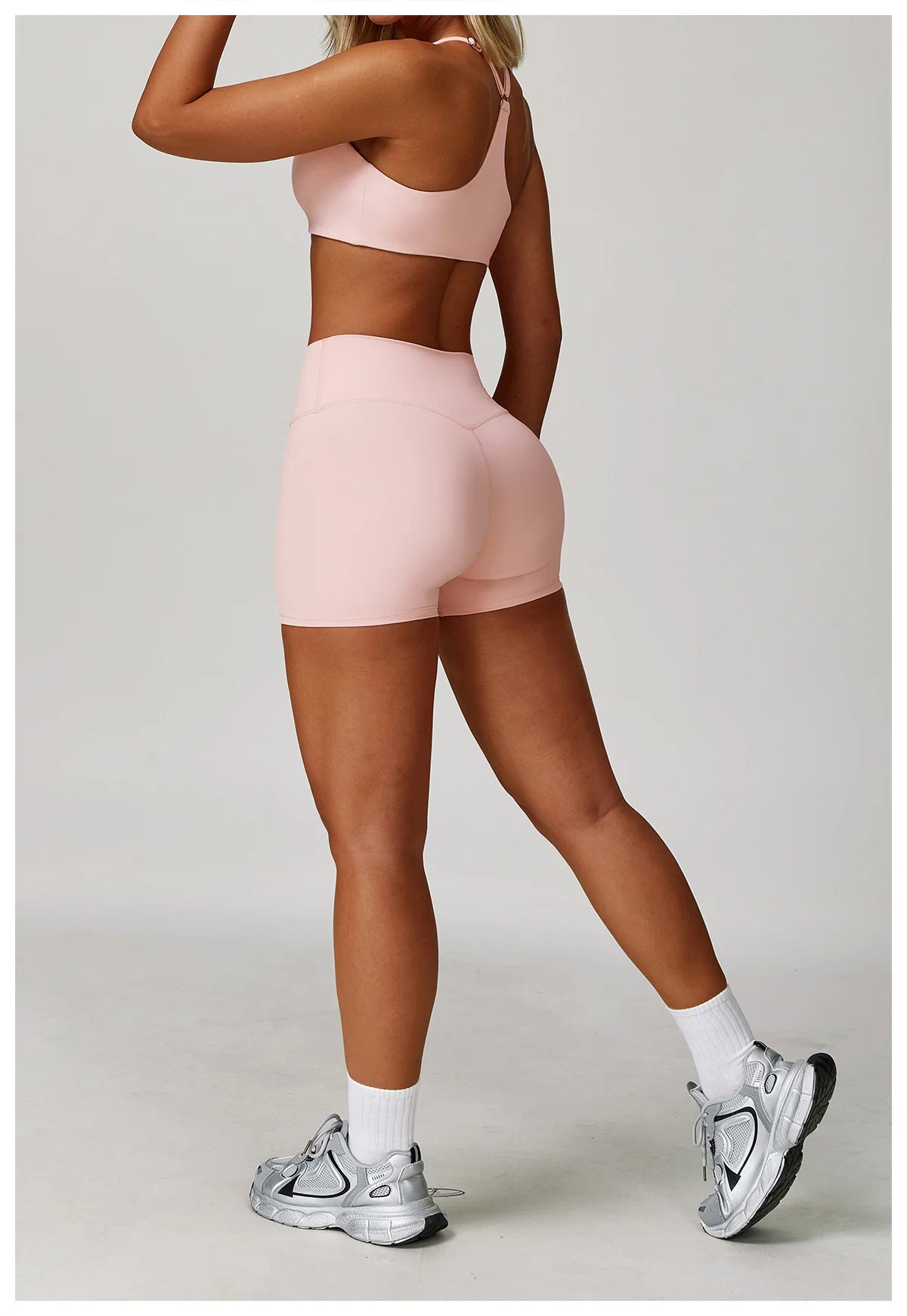 A woman models a pink 3-piece yoga sports set consisting of a crop top, brief, and shorts.