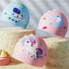 Three silicone swimming caps featuring space, a unicorn, and a dinosaur design displayed on textured surfaces.