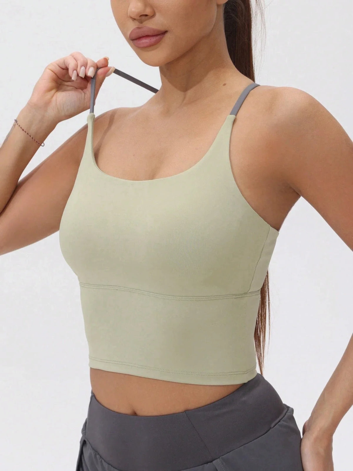 A model wearing a light olive green women's athletic crisscross tank top and dark gray athletic bottoms.