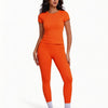 Una mujer modela un conjunto de yoga naranja sin costuras de tiro alto con top de manga corta y leggings largos.