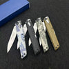 A collection of four precision folding pocket knives in various colors and finishes laid on a dark surface.