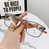 A hand holds a pair of TR90 sports reading glasses with brown frames and blue light protection on a white surface.