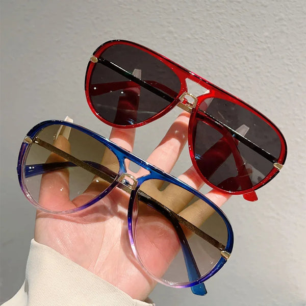 A hand holds a pair of vintage pilot sunglasses with gradient blue lenses and red frames.