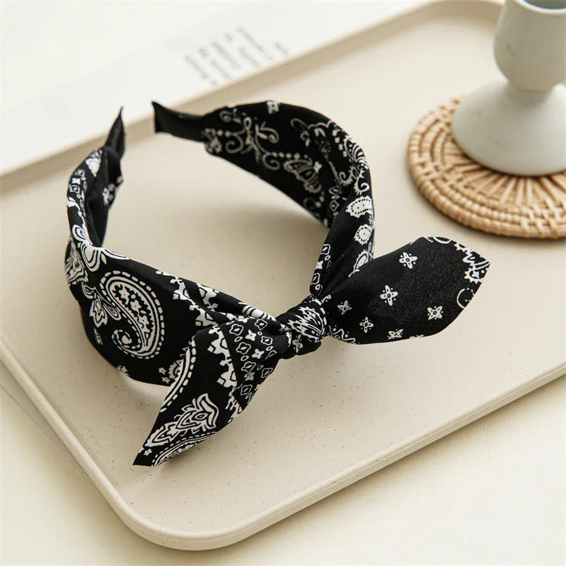 Black paisley bandana headband tied in a bow resting on a light tray.