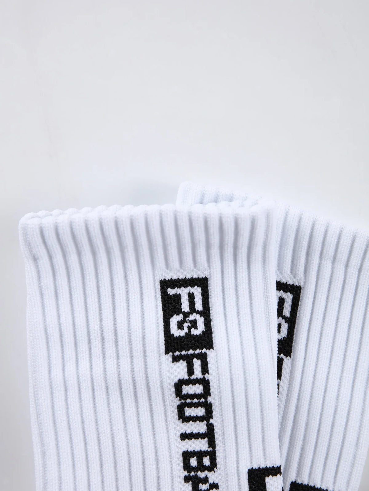A close-up of white men's athletic soccer socks with black text branding.
