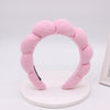 A pink sponge terry cloth headband for hair styling displayed on a white circular stand.