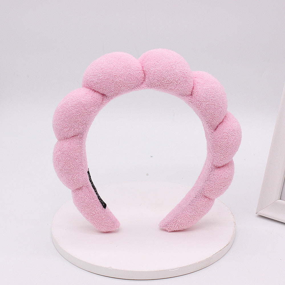 A pink sponge terry cloth headband for hair styling displayed on a white circular stand.
