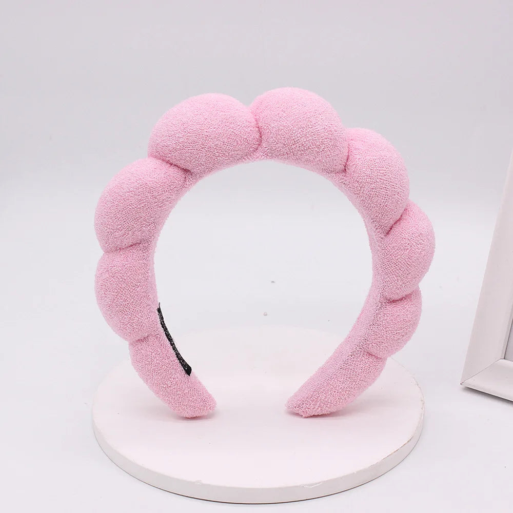 A pink sponge terry cloth headband for hair styling displayed on a white circular stand.