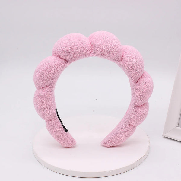 Un bandeau en tissu éponge rose pour le coiffage, exposé sur un support circulaire blanc.