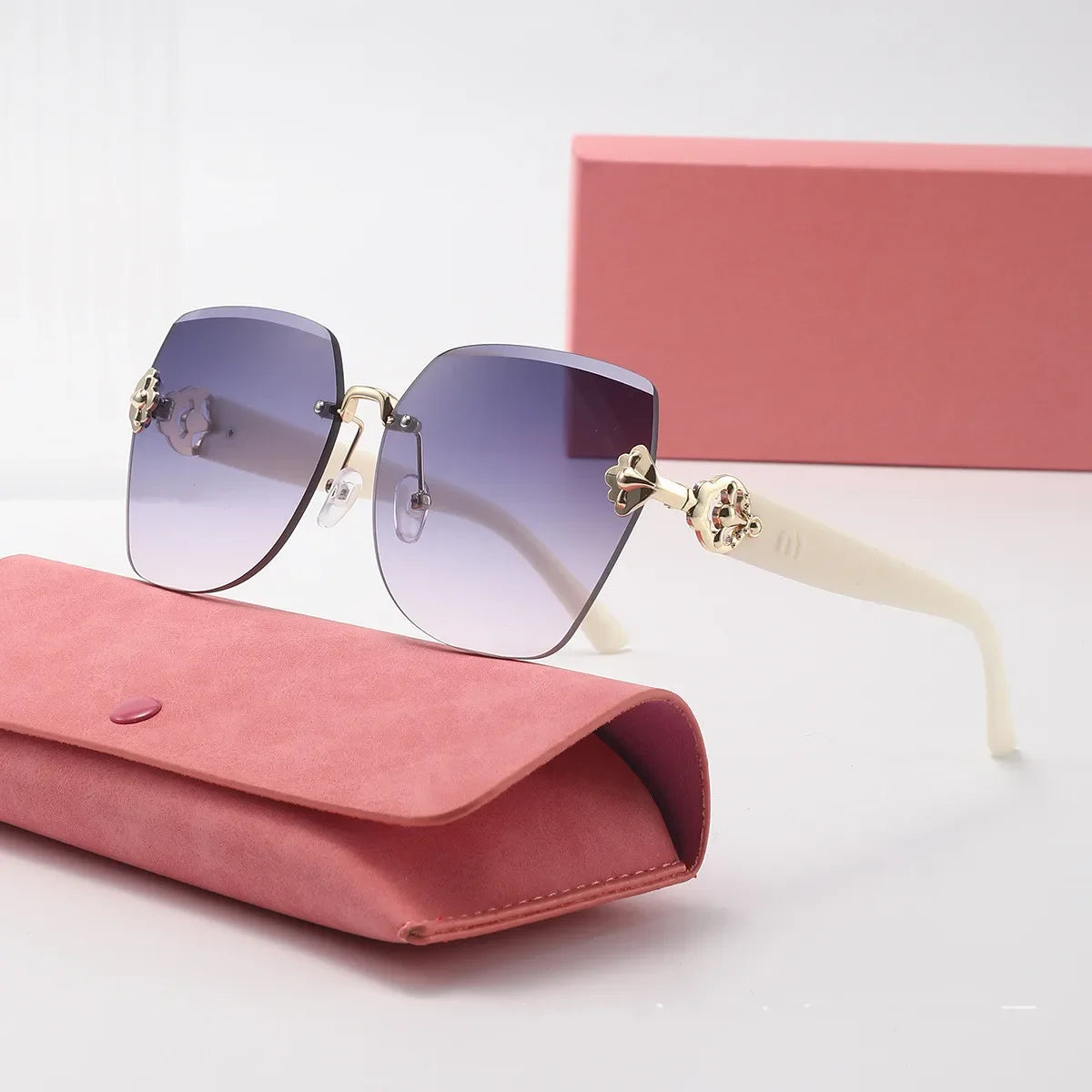 Light luxury frameless sunglasses with gold accents resting on a pink box and a matching pink pouch.