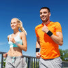 A woman and a man jogging outdoors wearing multi-sport breathable wristbands.