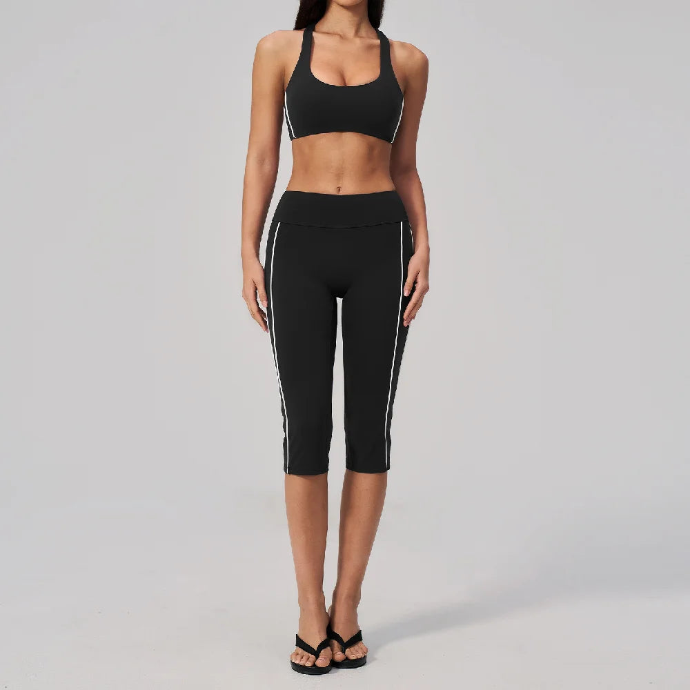 A woman models a black two-piece yoga and sports tracksuit set consisting of a cropped top and full-length leggings.