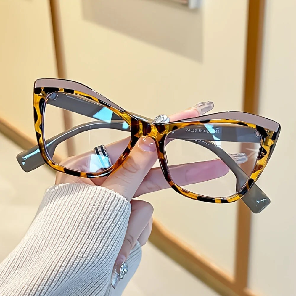 A hand holds a pair of vintage color block blue light blocking eyewear with tortoiseshell frames.