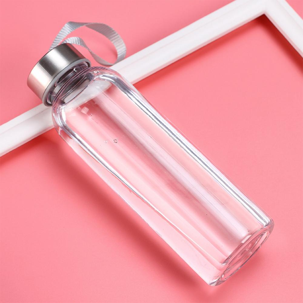 Une bouteille d'eau de sport en verre transparent avec un bouchon argenté et un ruban blanc sur un fond rose.