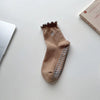 A pair of tan yoga socks with a ruffled cuff and studded toe, resting on a white surface.