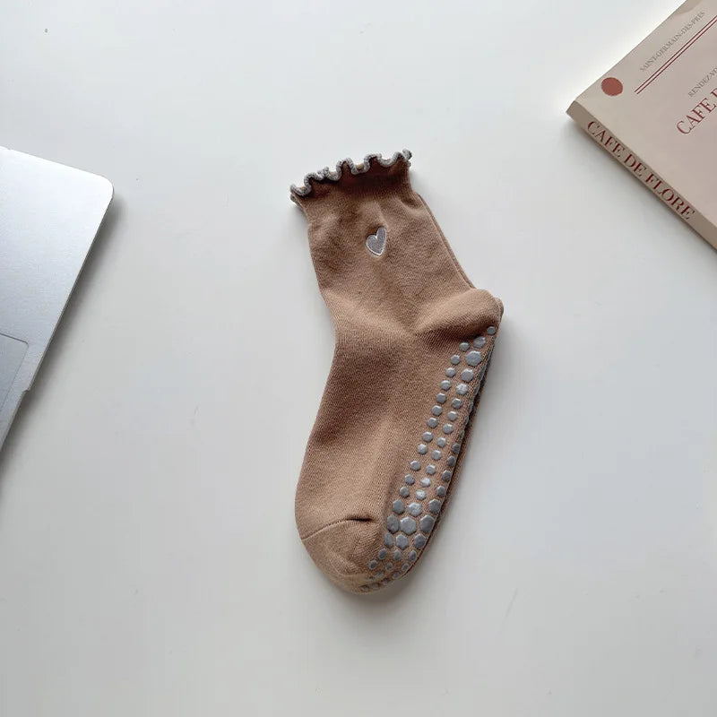 A pair of tan yoga socks with a ruffled cuff and studded toe, resting on a white surface.