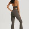 A woman wearing a dark olive green halter neck sports bra top and matching leggings poses against a light gray background.