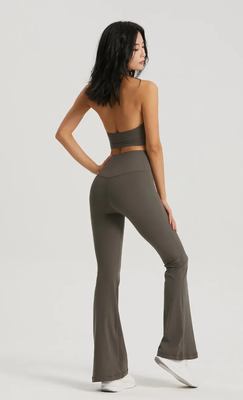 A woman wearing a dark olive green halter neck sports bra top and matching leggings poses against a light gray background.