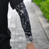 A close-up of a person wearing black clothing and a long sleeve tattoo featuring white designs on their arm.