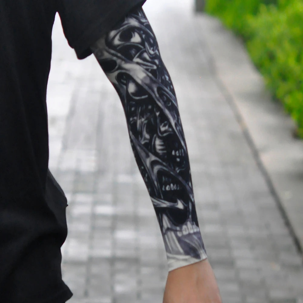 A close-up of a person wearing black clothing and a long sleeve tattoo featuring white designs on their arm.