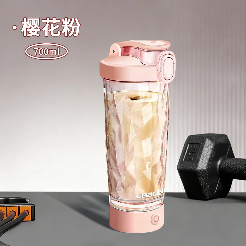 A pink portable electric shaker bottle filled with a yellowish liquid, shown next to a black shaker attachment.