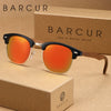 Un par de gafas de sol retro BARCUR tintadas en naranja, apoyadas en una caja de cartón marrón.