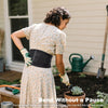 Eine Frau in einem Blumenkleid beugt sich, um einen Garten anzupflanzen und demonstriert eine ergonomische Lendenstütze.